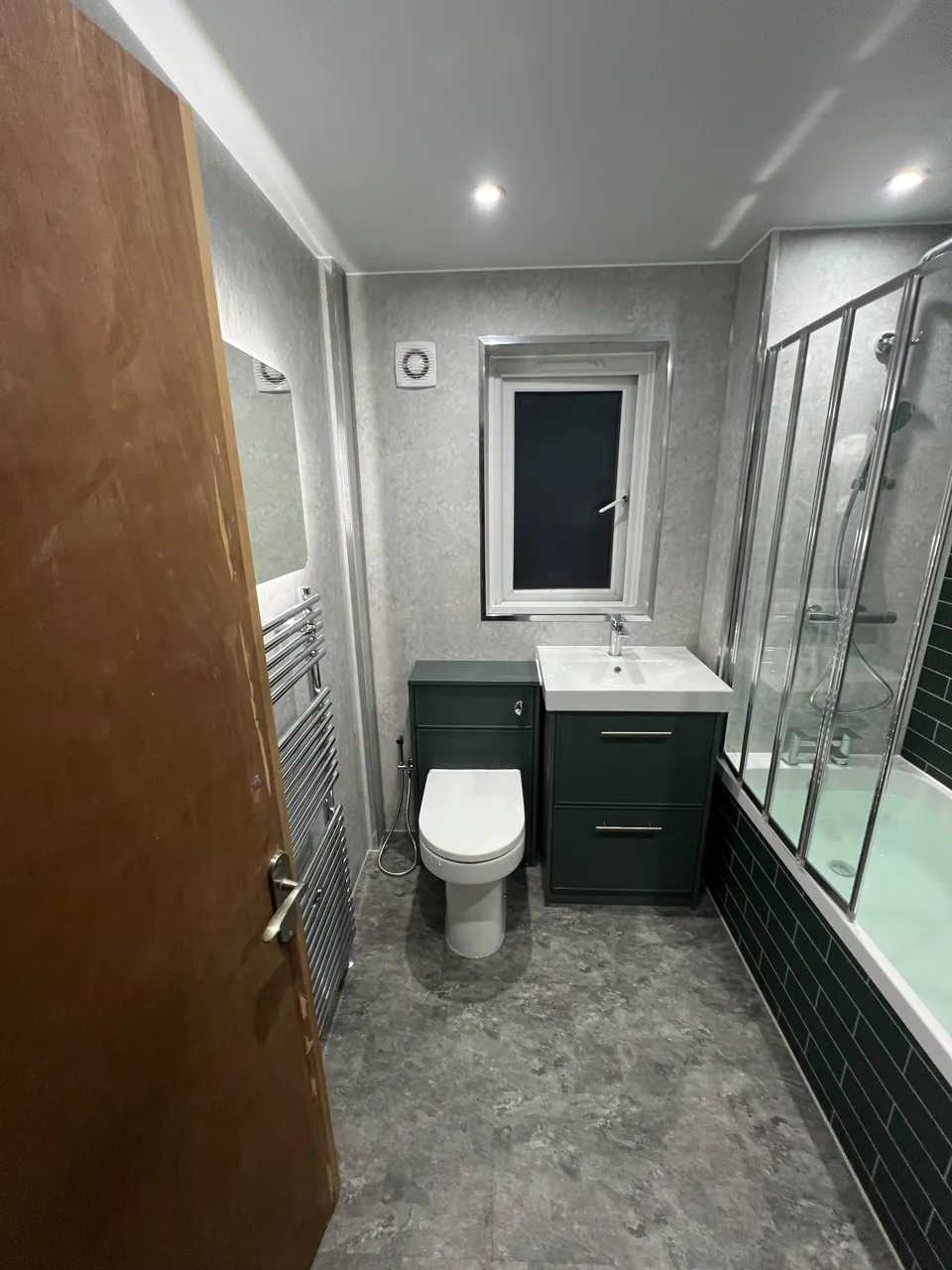 Green-tiled bath with shower screen and fitted storage